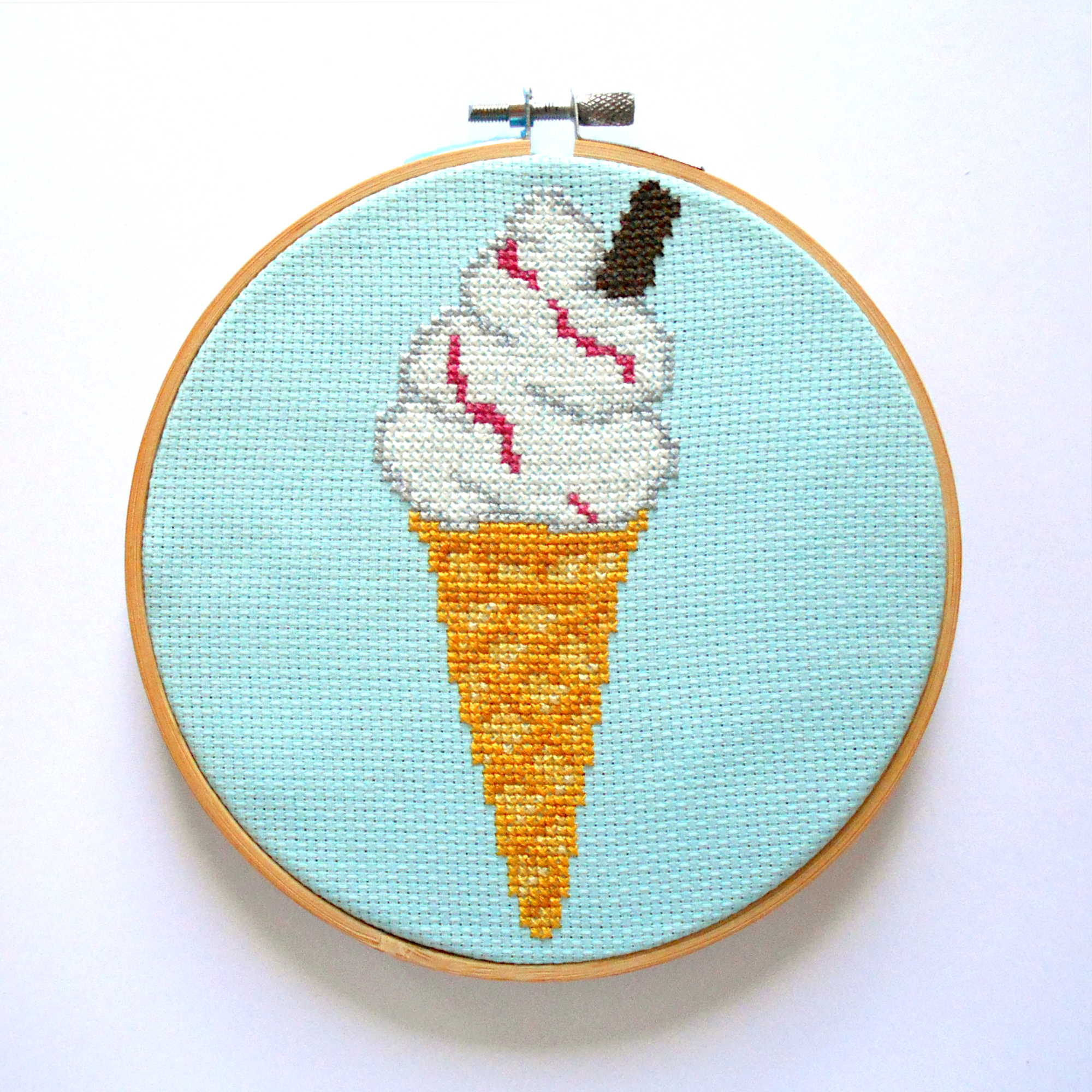 Cross stitch of a Mr Whippy ice cream cone with a flake (a 99) and sauce displayed in an embroidery hoop