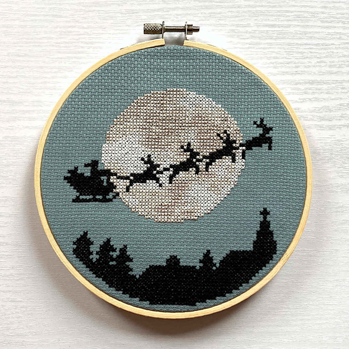 Cross stitch of santa in his sleigh pulled by reindeer silhouetted against the moon