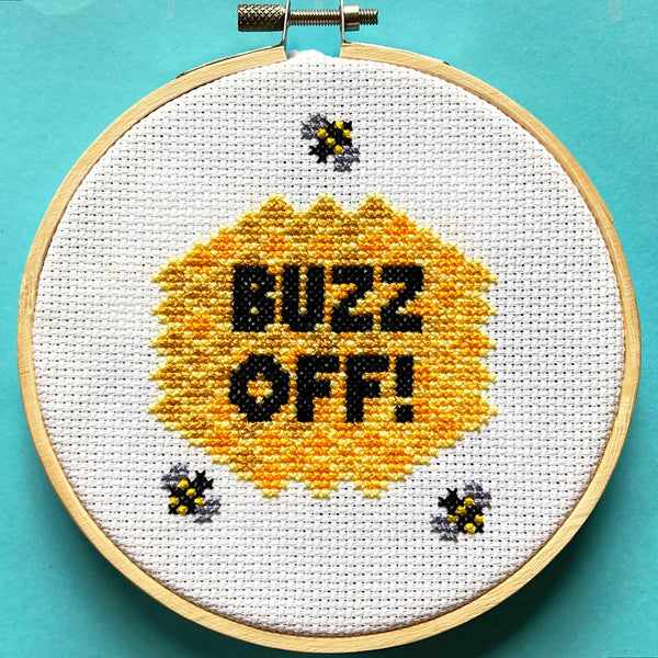 Cross stitch of "buzz off" surrounded by honeycomb and bees in a 5 inch embroidery hoop